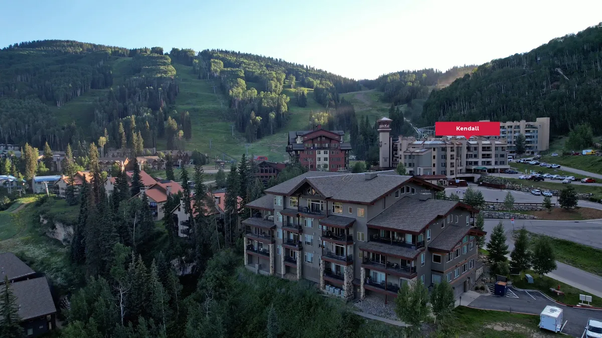A sweeping exterior view displaying majestic mountains, lush trees, and the architecture of nearby buildings. The landscape reflects both adventure and peaceful retreat, tying together the allure of outdoor exploration and the comfort of the surrounding lodge environment.