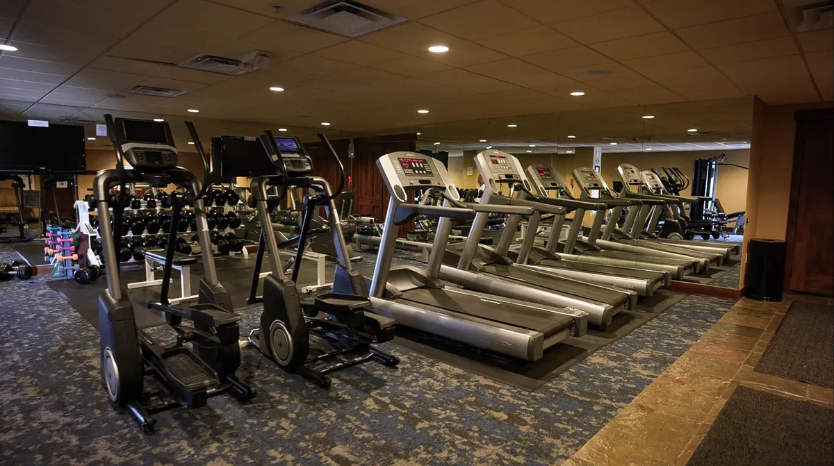 A modern fitness center equipped with treadmills, ellipticals, free weights, and mirrors. The space appears bright and motivating, with ample natural light and clean design, ideal for personal workouts or group fitness activities.