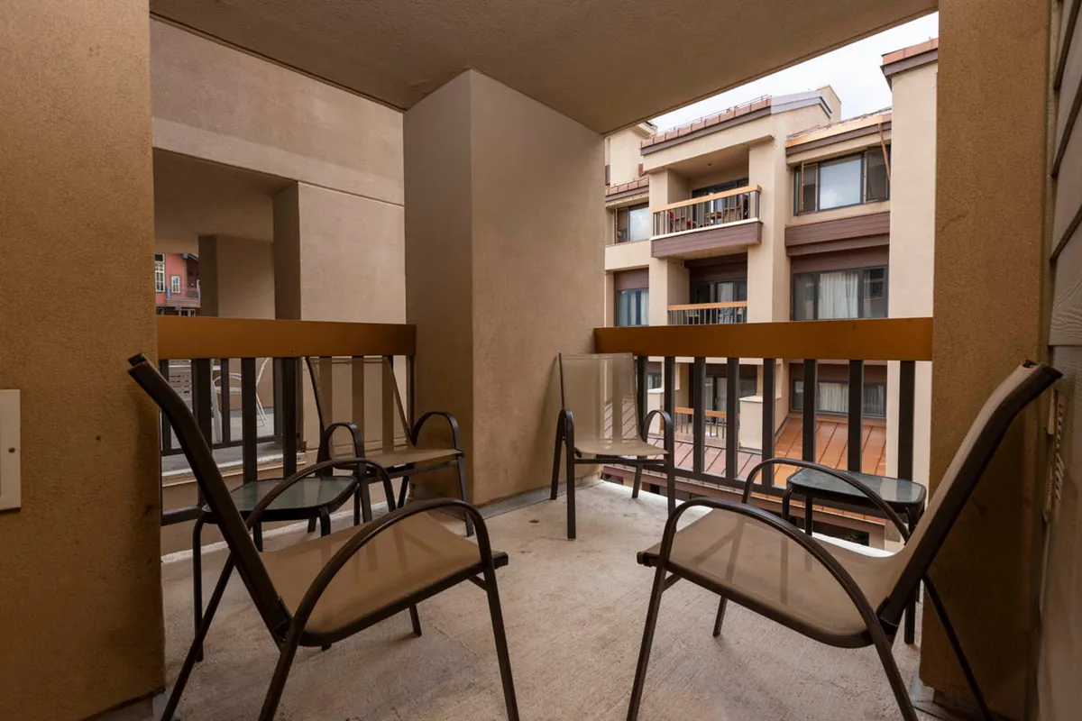A cozy balcony with inviting chairs and a railing, perfectly set up for relaxing, enjoying drinks, or quietly soaking in the mountain air while observing the lively Village Plaza below.